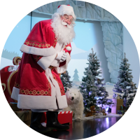 Santa telling a story to children in front of sleigh and trees.